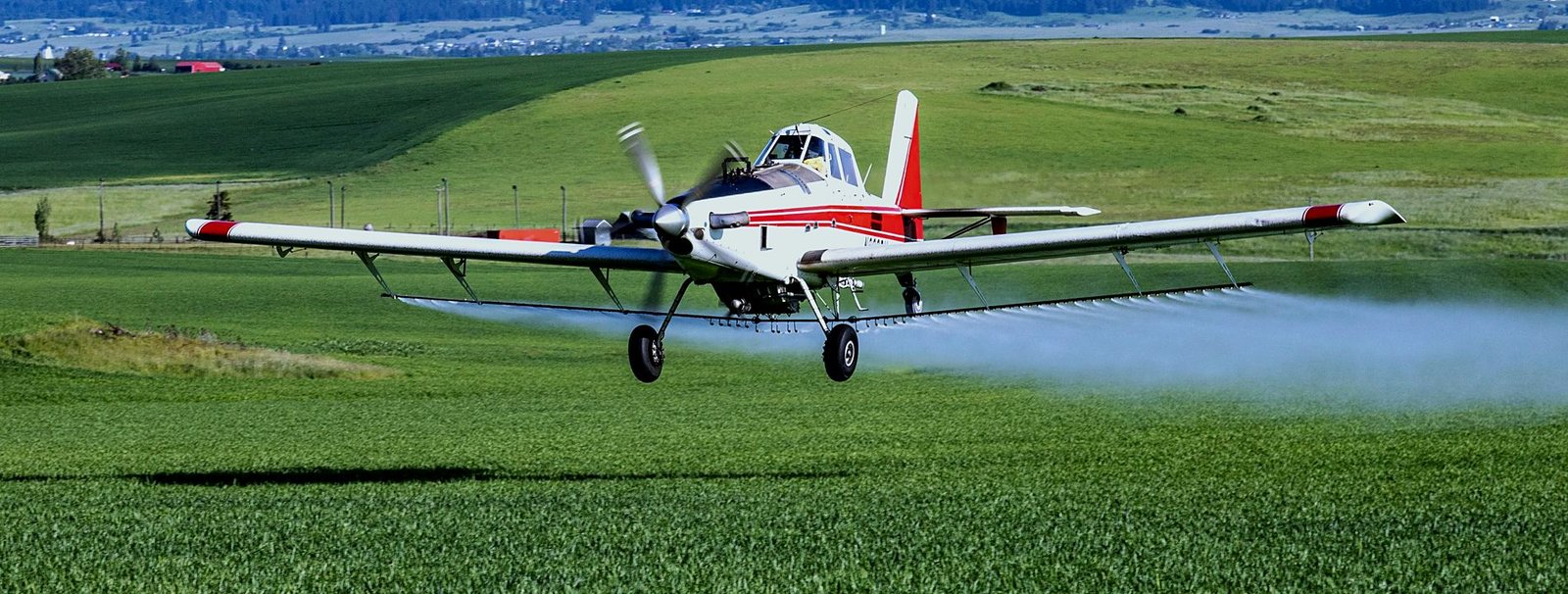 Spray boom releasing over a green field from a low-flying ag aircraft